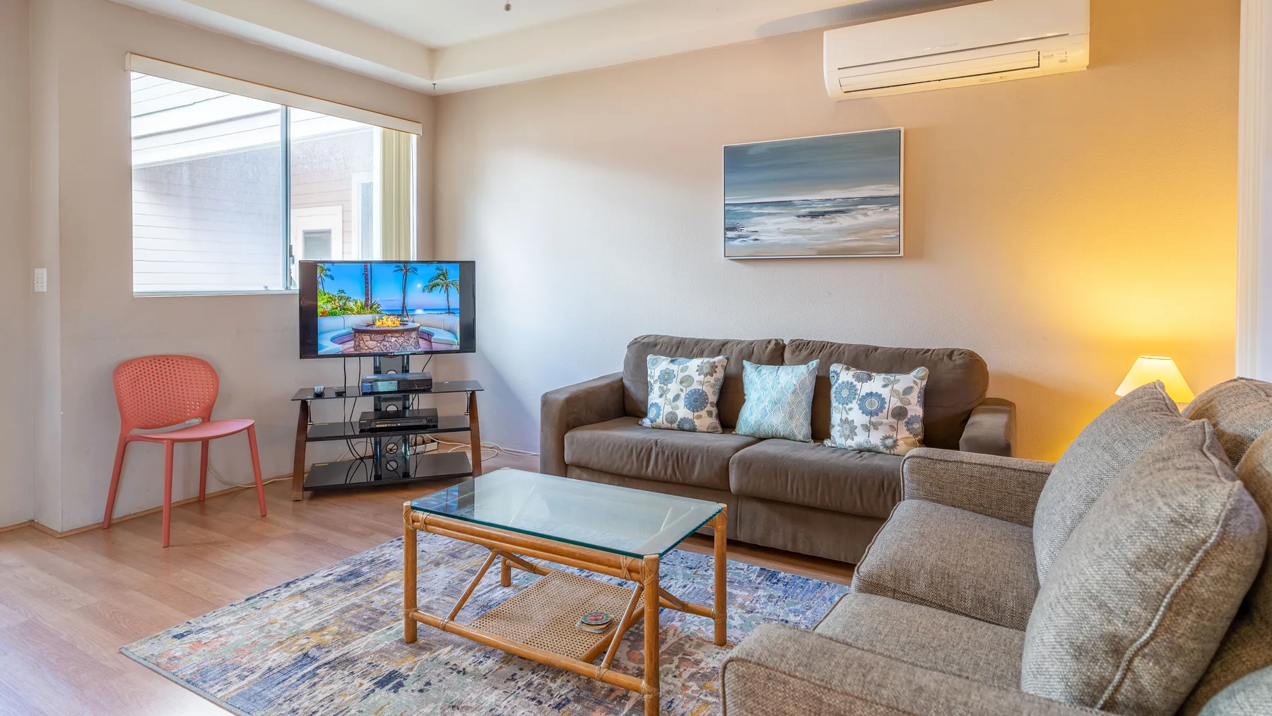 Una sala de estar con asientos, una mesa de centro y un televisor junto a la ventana.