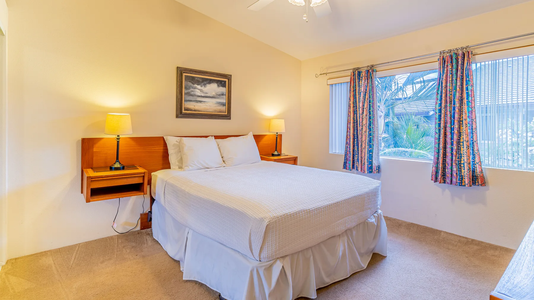 A bright bedroom with a bed beneath a window dressed with colorful curtains.