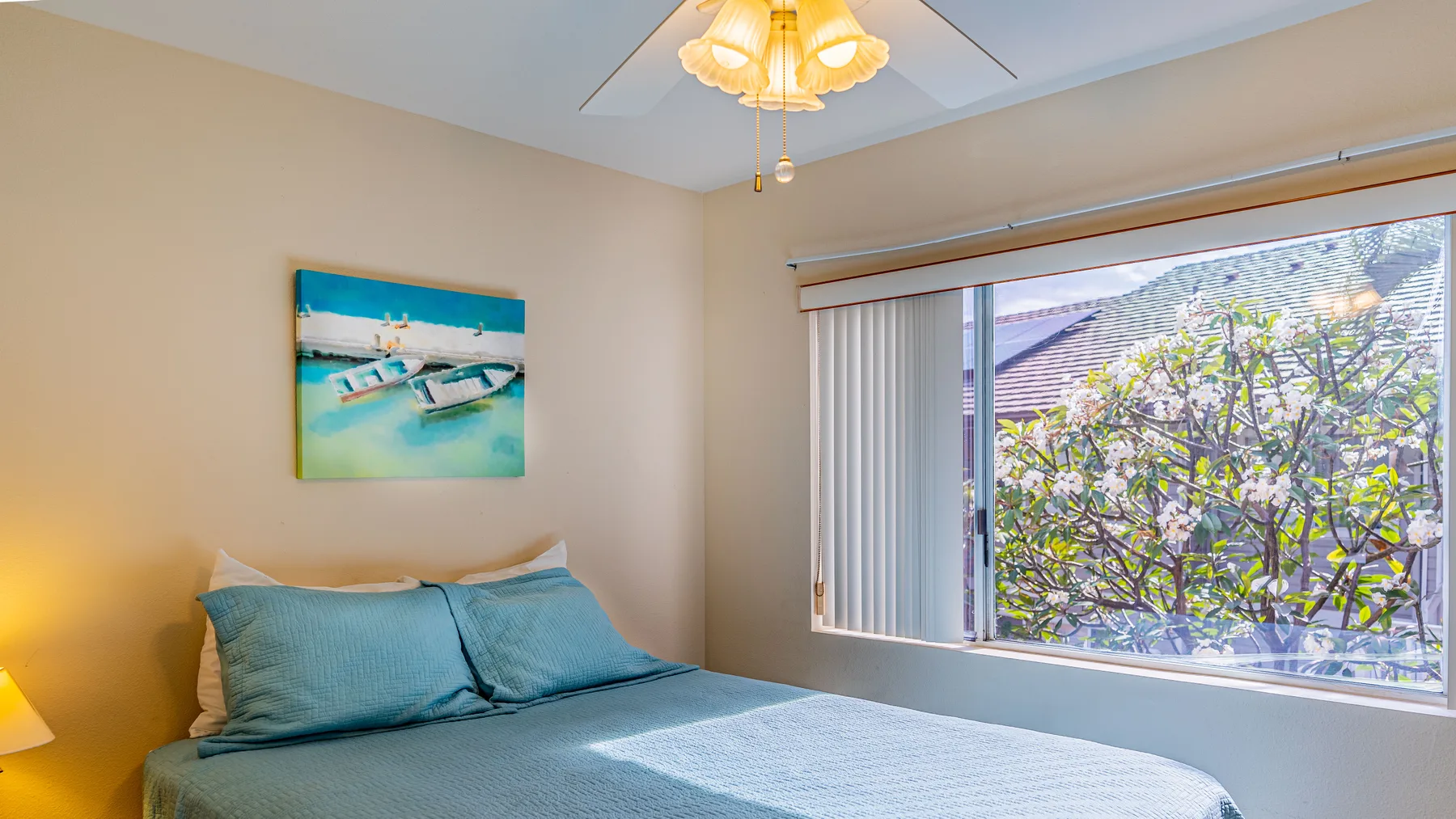 A bedroom with a bed beside a large window overlooking leafy branches.