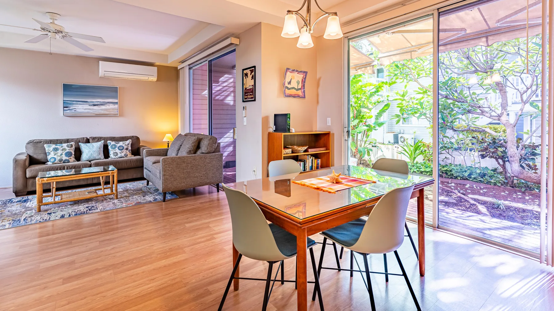Sala de estar y comedor con asientos junto a grandes puertas de vidrio y vegetación.