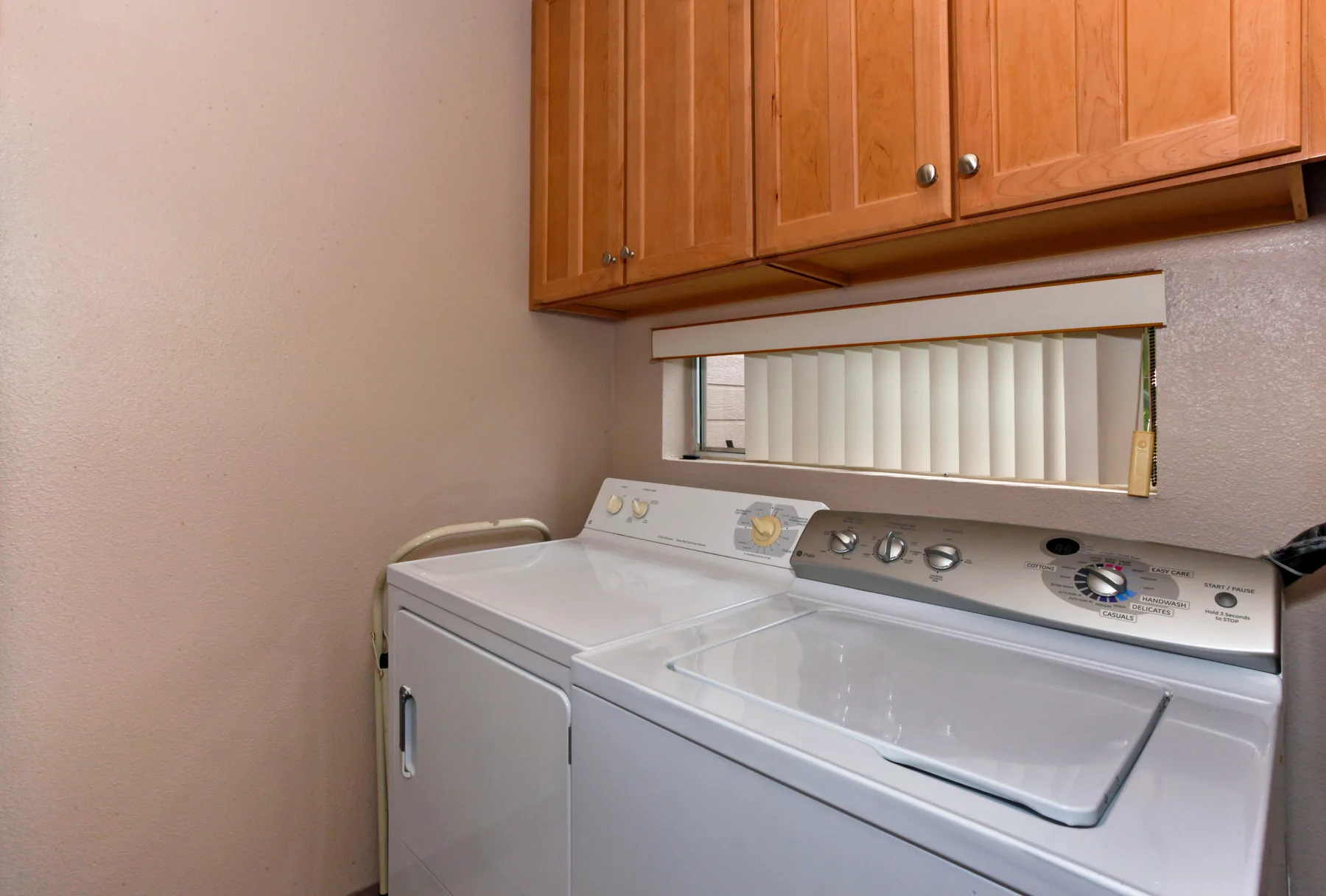 A laundry area with a washer and dryer beneath wooden cabinets.