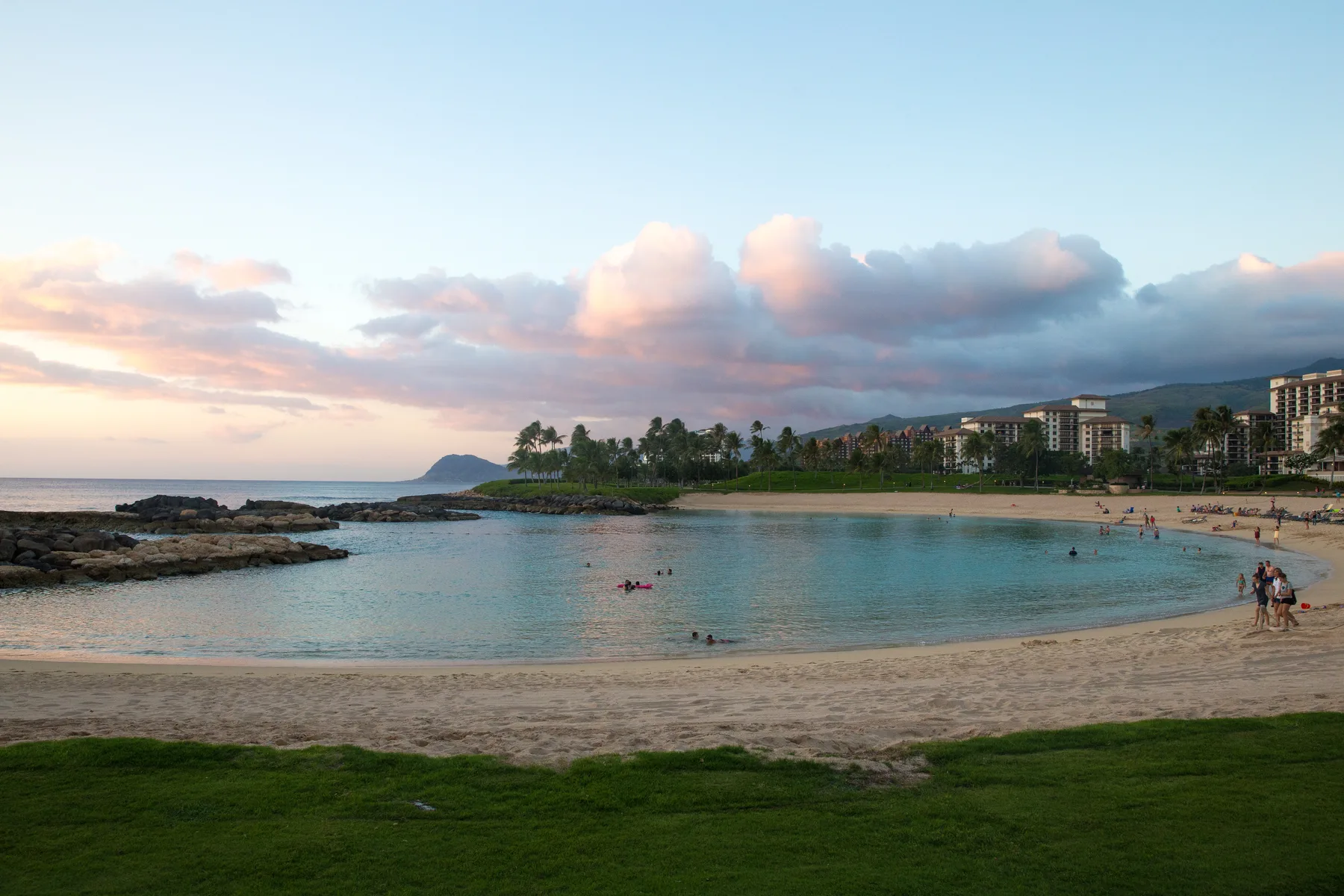 A coastal beach and calm bay sit beneath a cloudy evening sky.