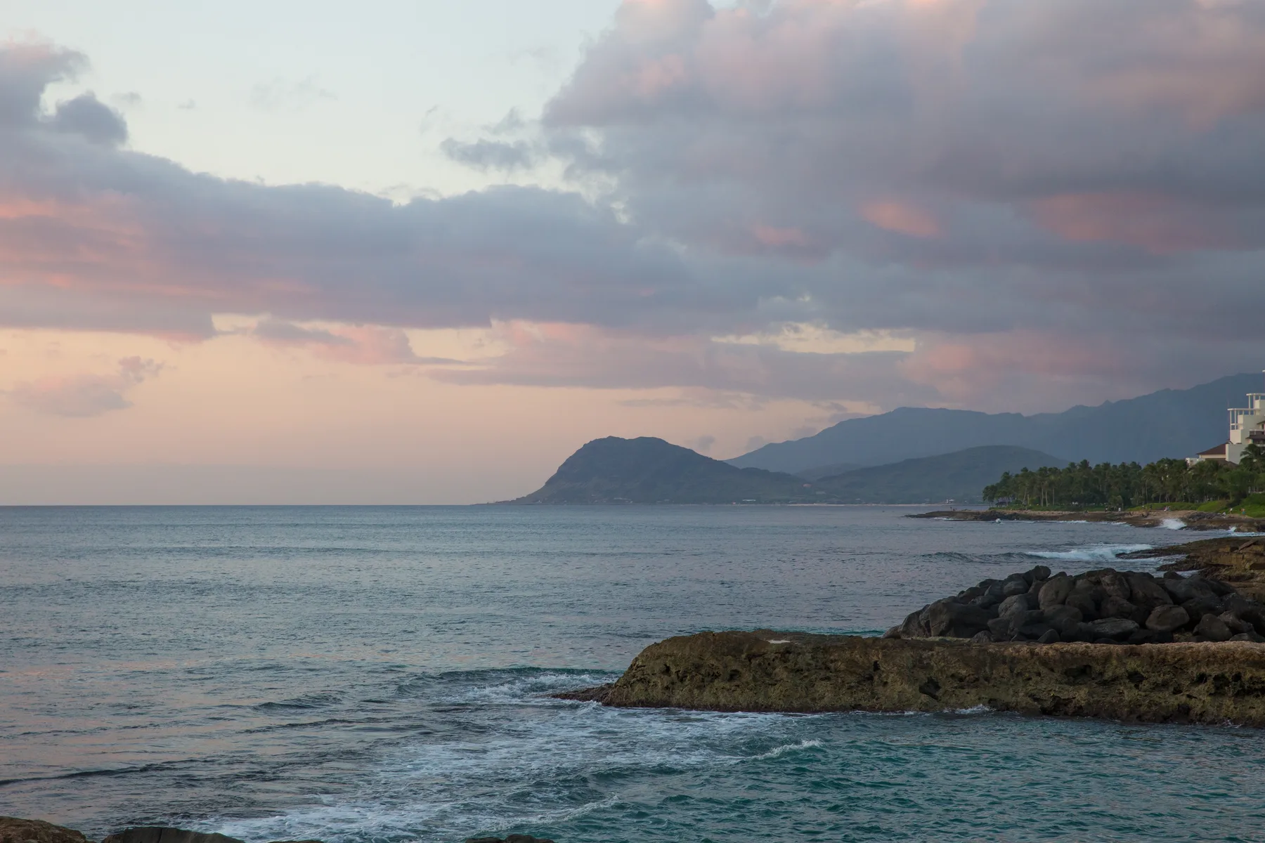 A coastal seascape at dusk, with waves washing over a rocky shoreline.