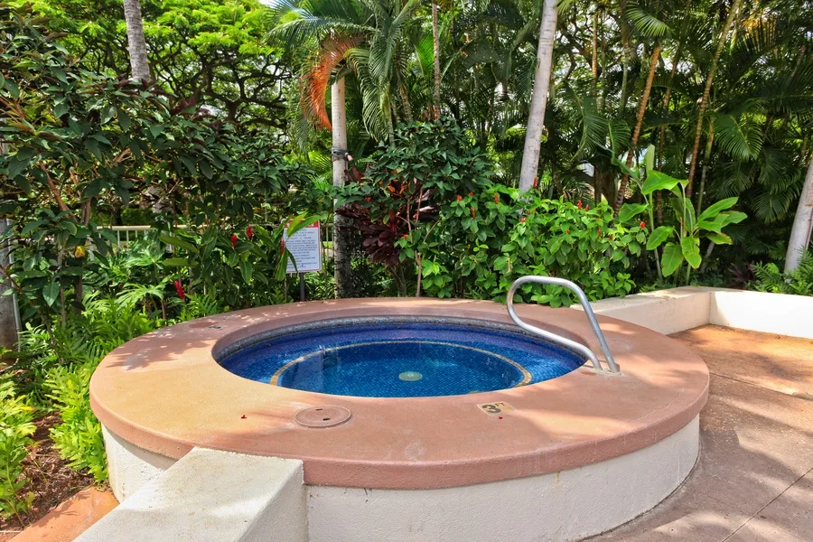 A circular outdoor spa sits on a paved patio surrounded by tropical greenery.