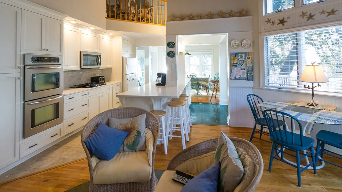 Una luminosa cocina-comedor de planta abierta, con una isla central y una mesa junto a las ventanas.