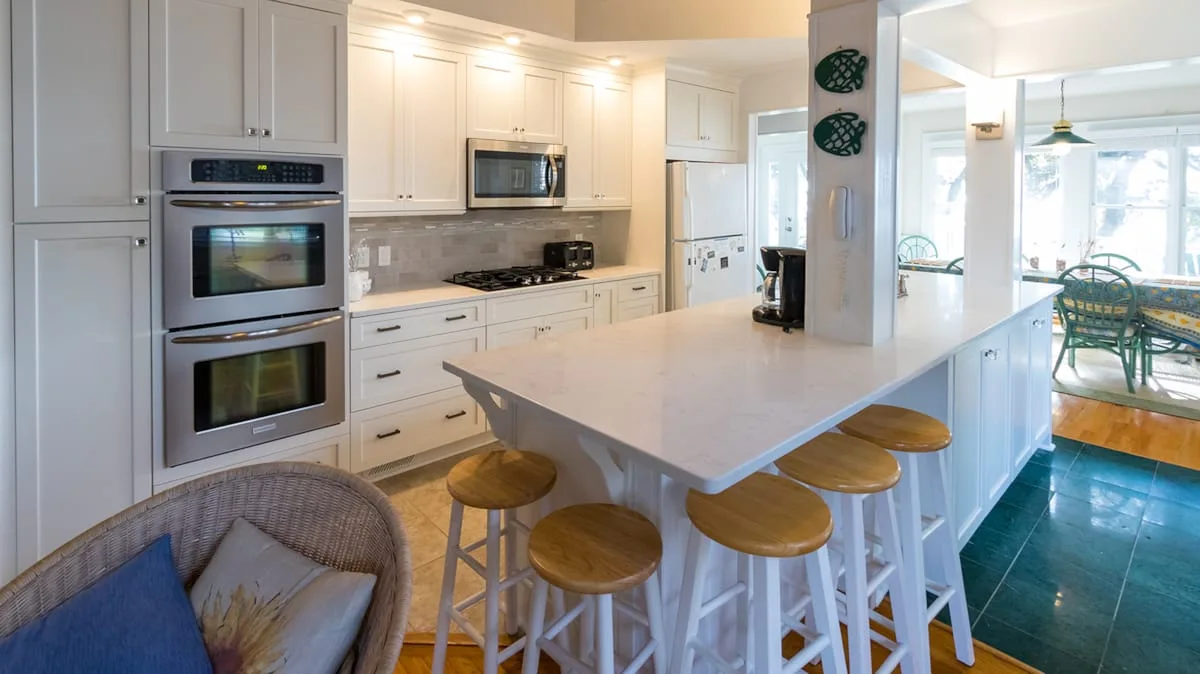 Una cocina luminosa con una isla grande y taburetes se abre a un comedor.