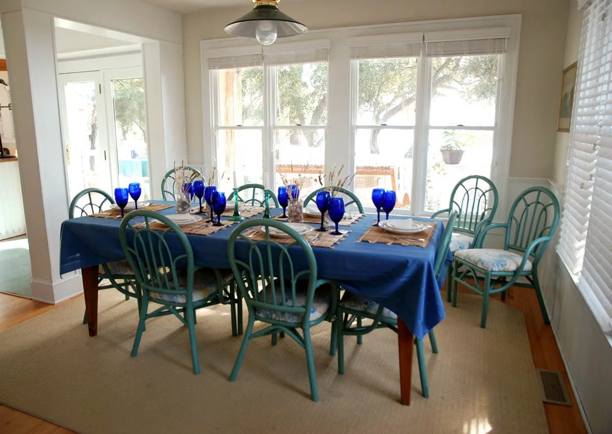 Un comedor con una mesa larga puesta con cristalería azul y rodeada de sillas.