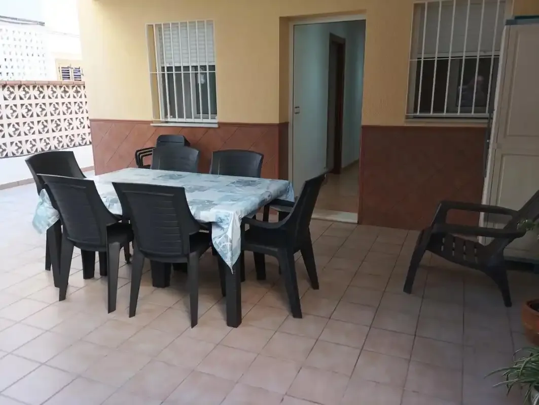 A tiled patio has a table with a cloth and several chairs.