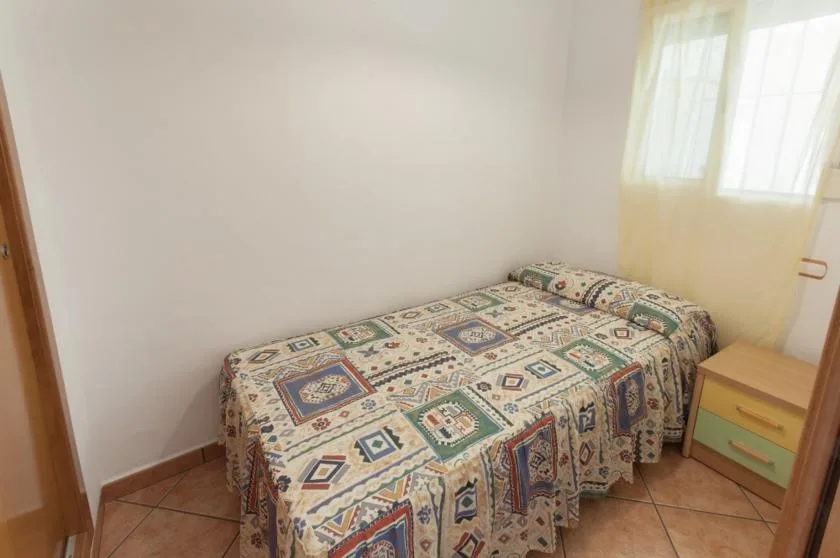 A bedroom with a single bed covered by a colorful patterned bedspread beside a window.