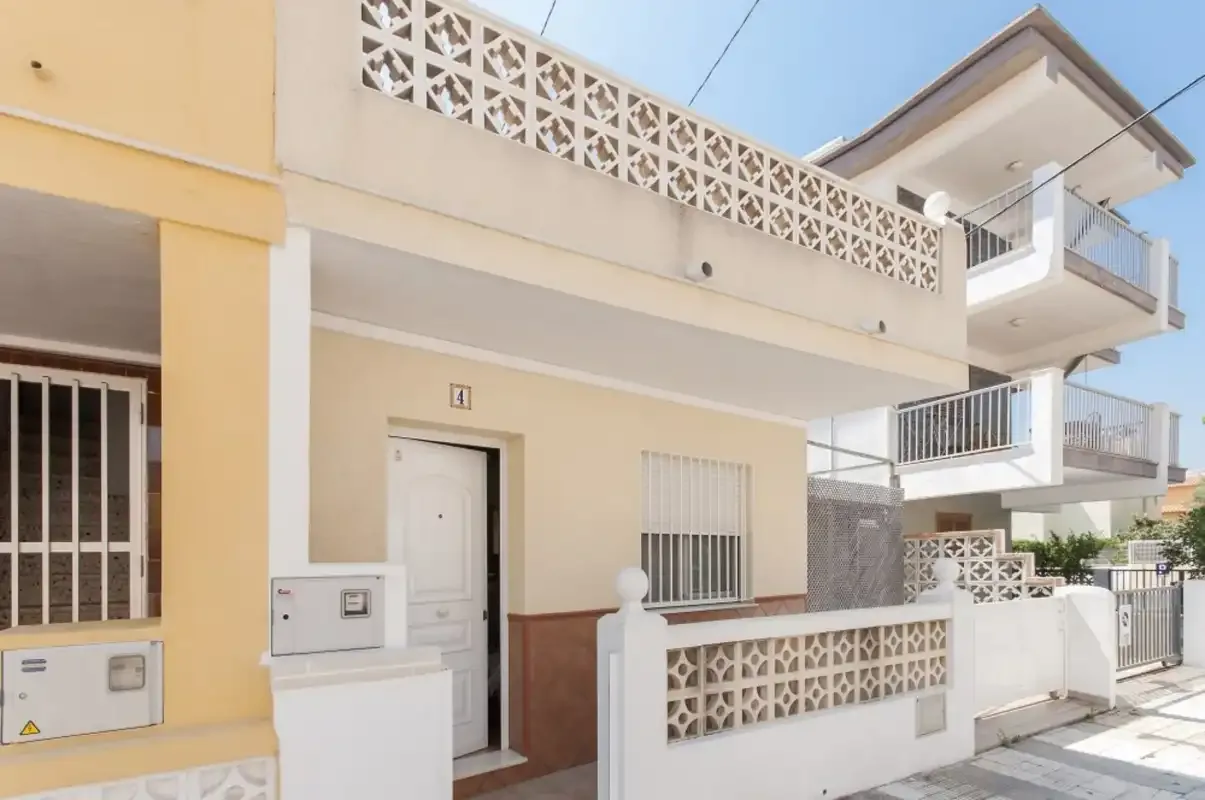 Street-facing residential building with a white entrance door and patterned boundary wall.