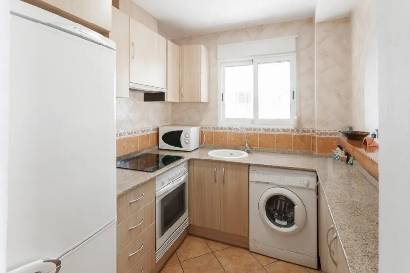 A compact kitchen with a washing machine beneath the counter and a window above the sink.