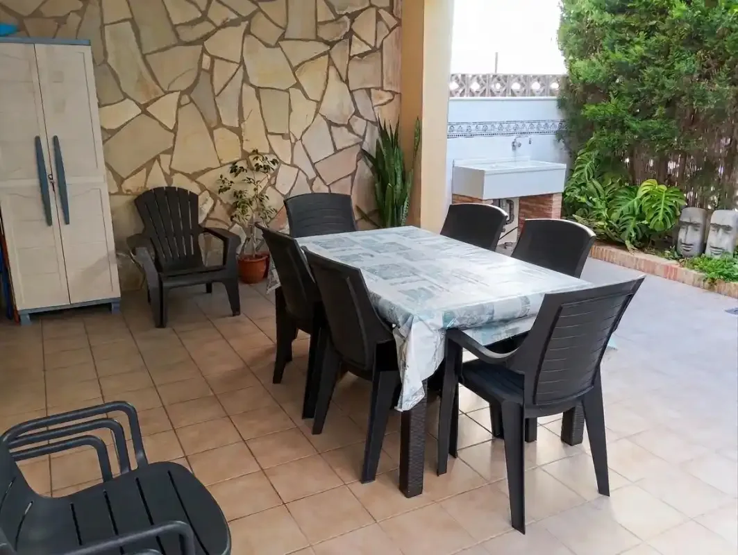 A tiled outdoor dining area with a table, dark seating, and garden greenery.
