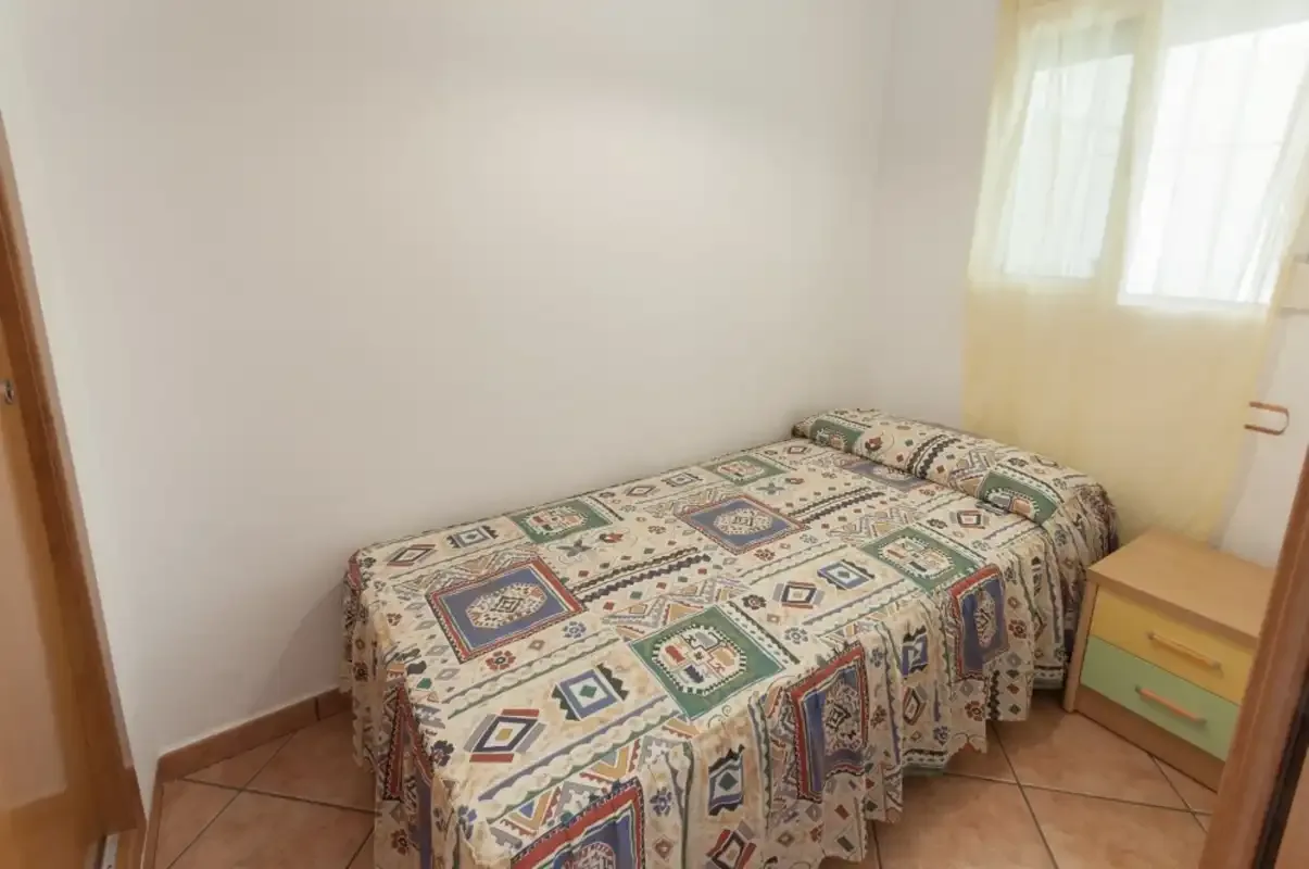 A small bedroom with a bed covered by a patterned bedspread beside a window.