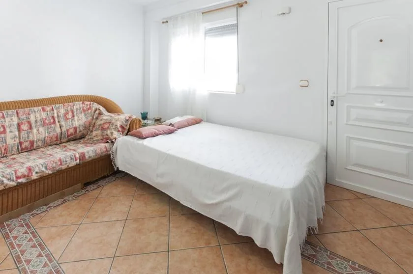 A bedroom with a bed beside a patterned sofa and a bright window.