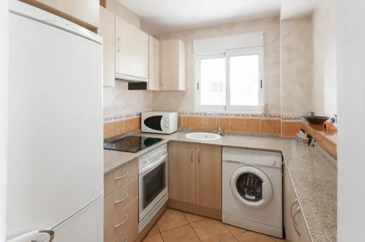 A compact kitchen with light wood cabinets, a refrigerator, and a washing machine.