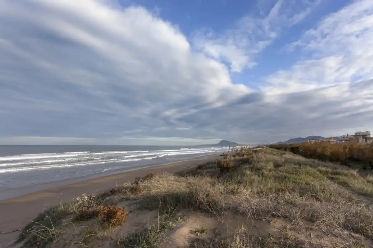 A sandy beach and coastal dunes stretch beside the sea under a cloudy sky.