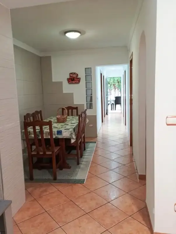A dining area with a table and chairs opens onto a tiled hallway.
