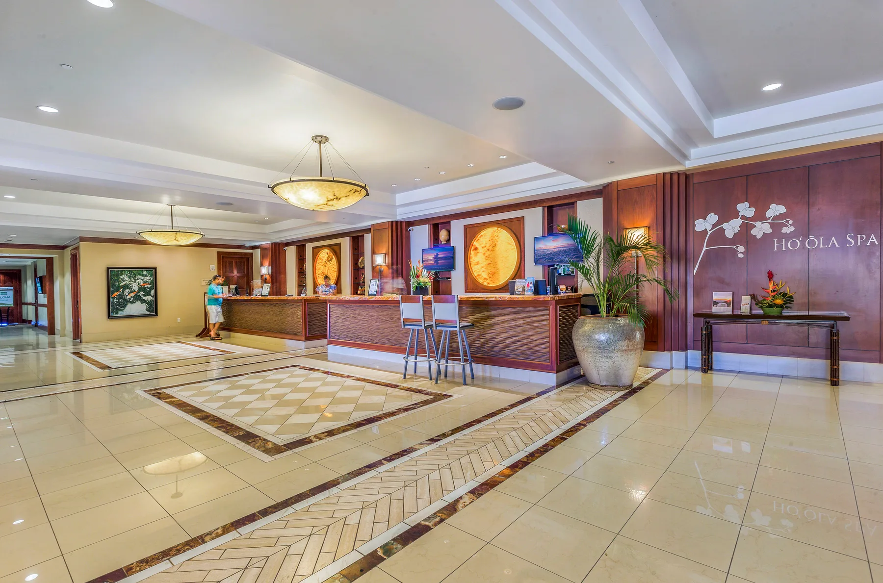 Un amplio vestíbulo de hotel cuenta con recepción, suelo de baldosas pulidas y una zona de asientos.
