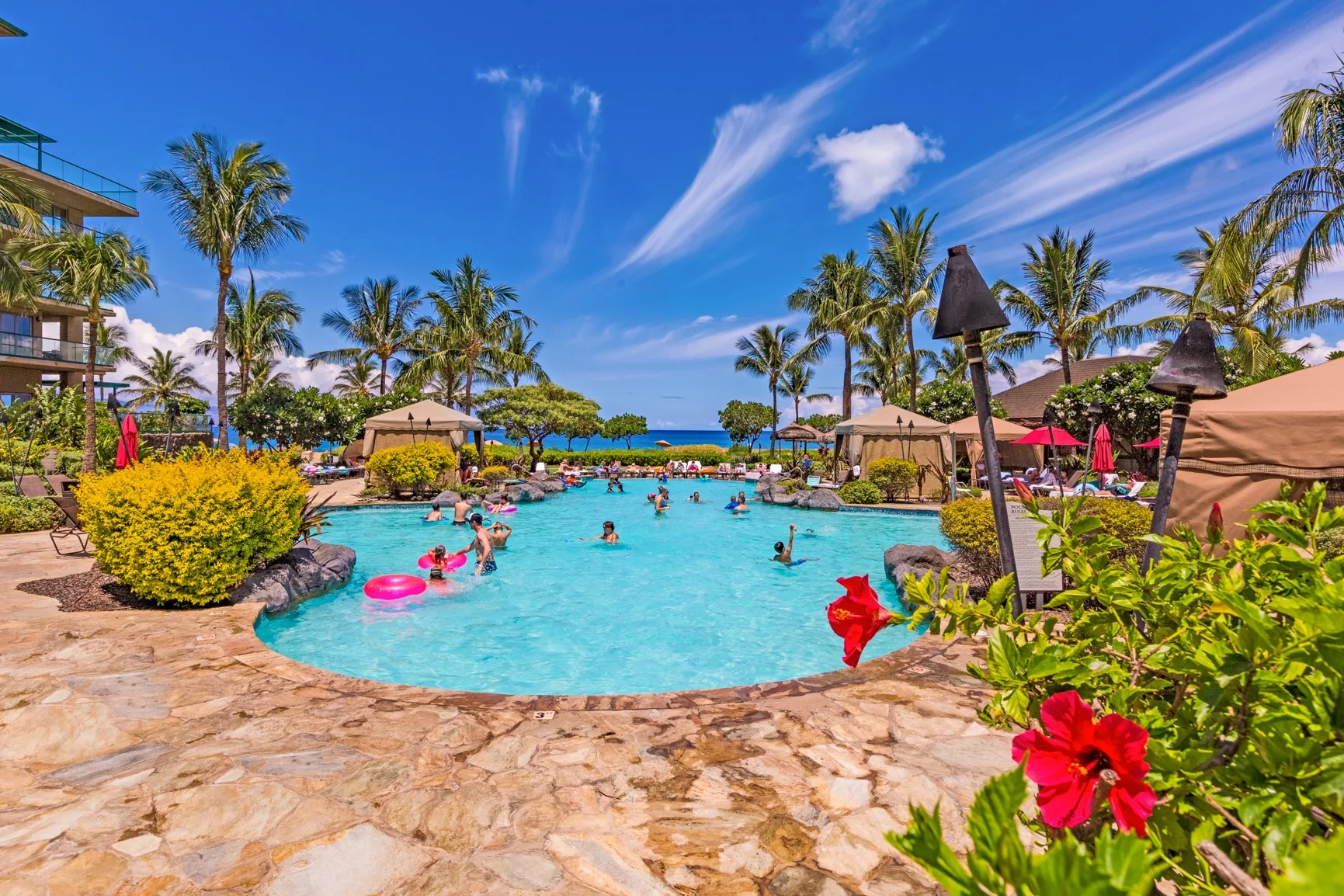 Una piscina de resort rodeada de palmeras, plantas y zonas de descanso.