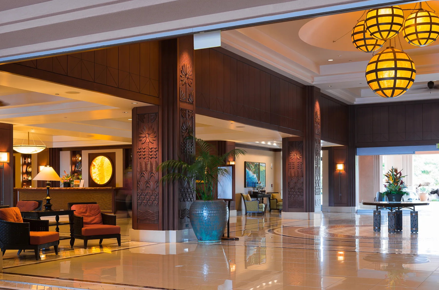 Un amplio vestíbulo de hotel con columnas de madera oscura, asientos y lámparas colgantes iluminadas.