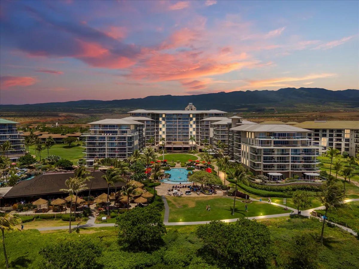Un complejo turístico rodea una piscina central y jardines bajo un cielo colorido al atardecer.