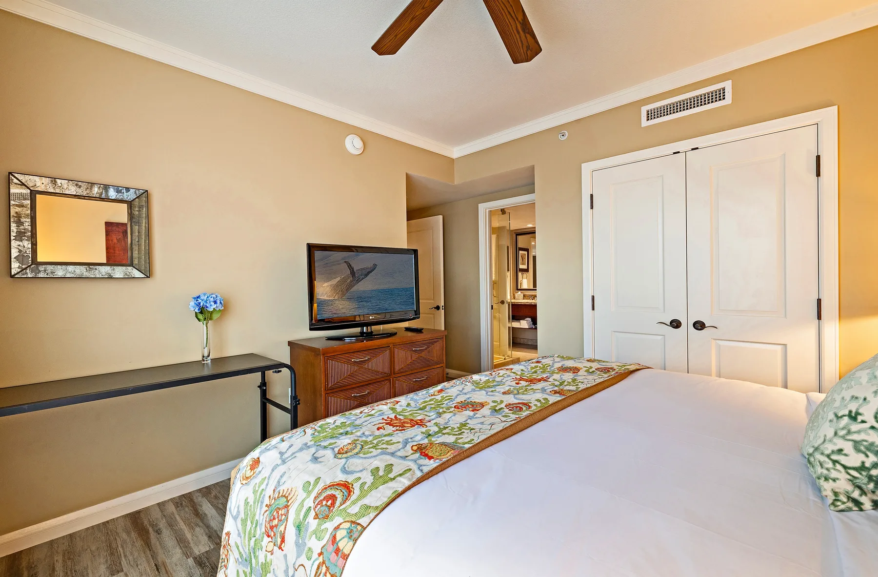Un dormitorio con una cama cubierta por una colcha floral colorida y un televisor sobre una cómoda de madera.