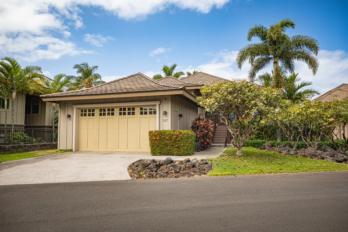 A house exterior with a garage, driveway, and tropical landscaping.