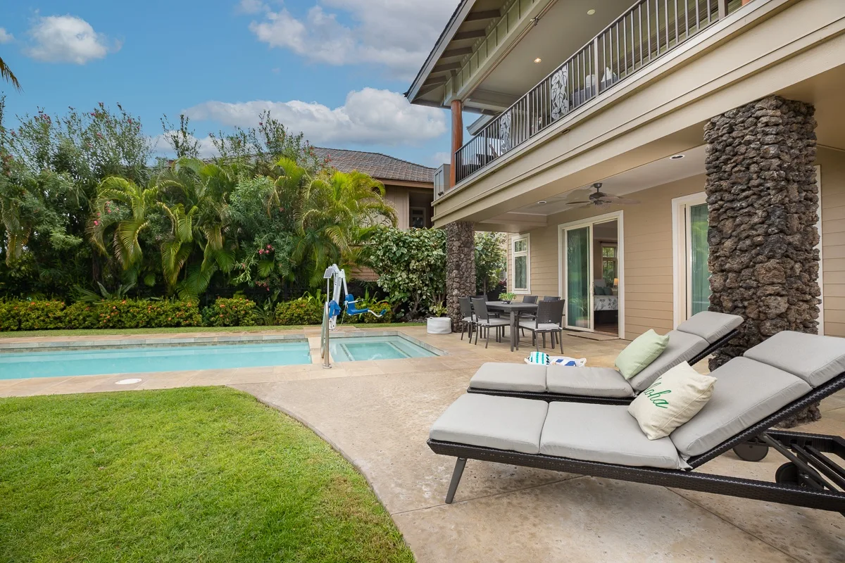 An outdoor pool and patio beside a two-story house, with lounge seating.