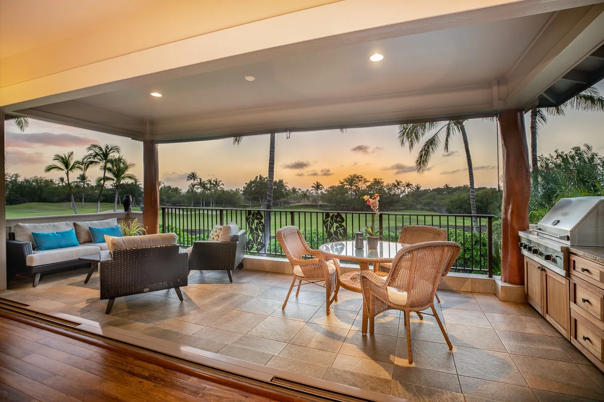 Un patio cubierto con asientos al aire libre, una mesa y vistas a la vegetación al atardecer.