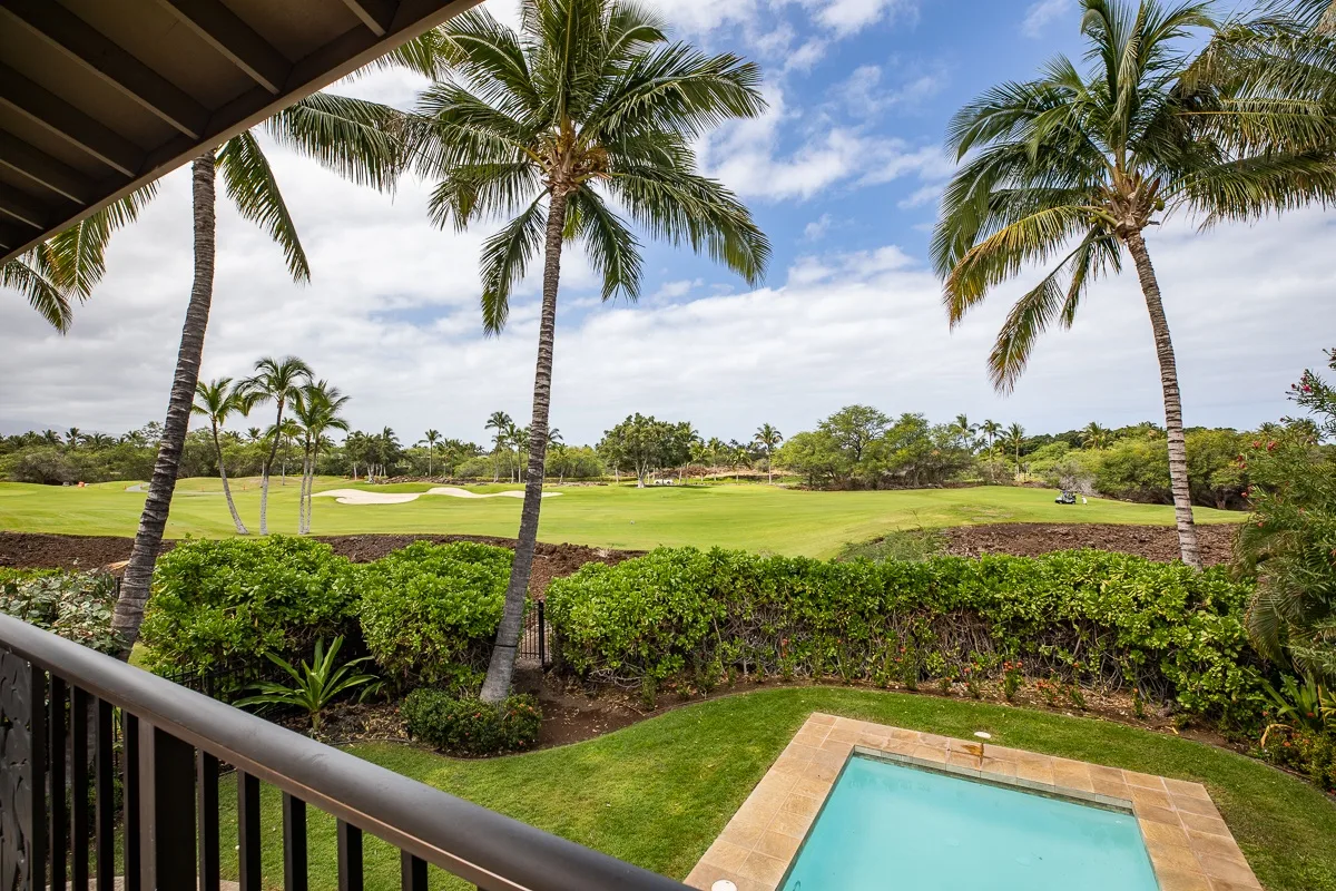 A balcony overlooks a swimming pool, palm trees, and a green golf course.