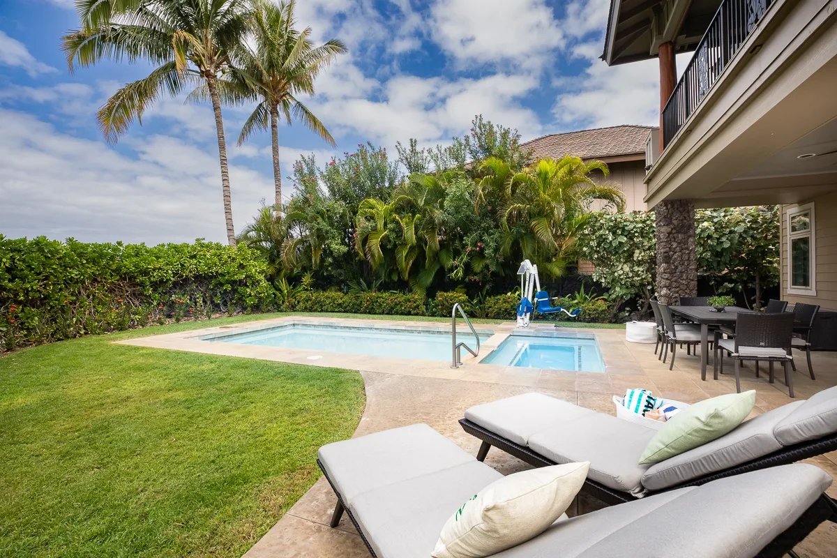Piscina y patio traseros con asientos, vegetación y palmeras.