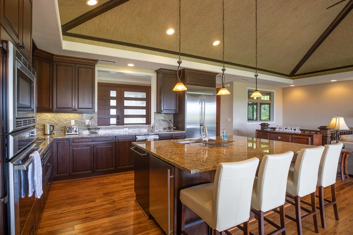 A spacious kitchen with a central island, pendant lights, and white seating.