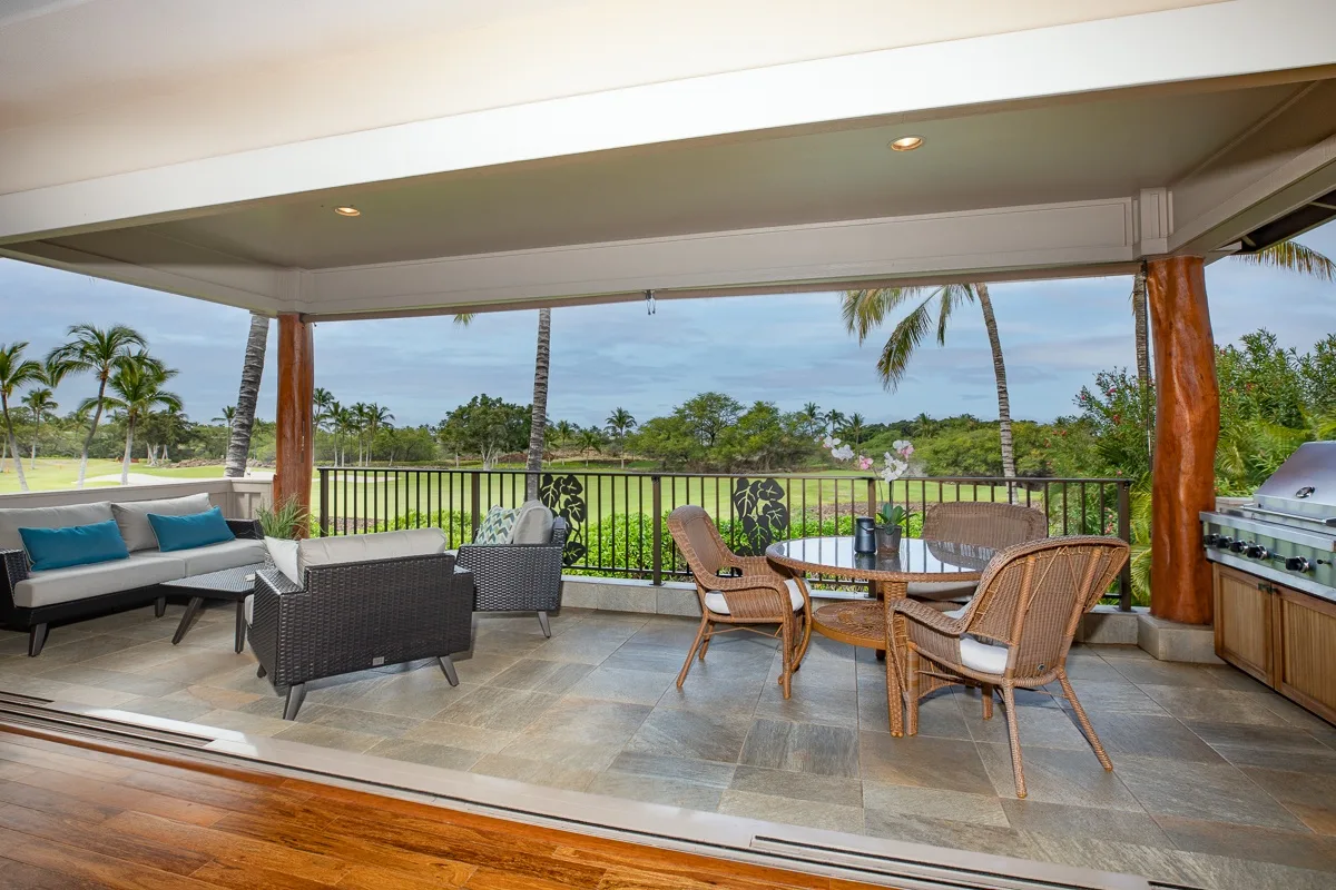 A covered patio with outdoor seating overlooks palm trees and greenery.