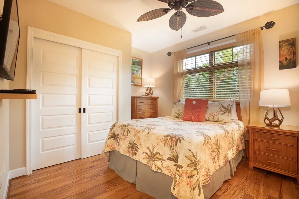 A bedroom with a bed beneath a wide window with blinds.