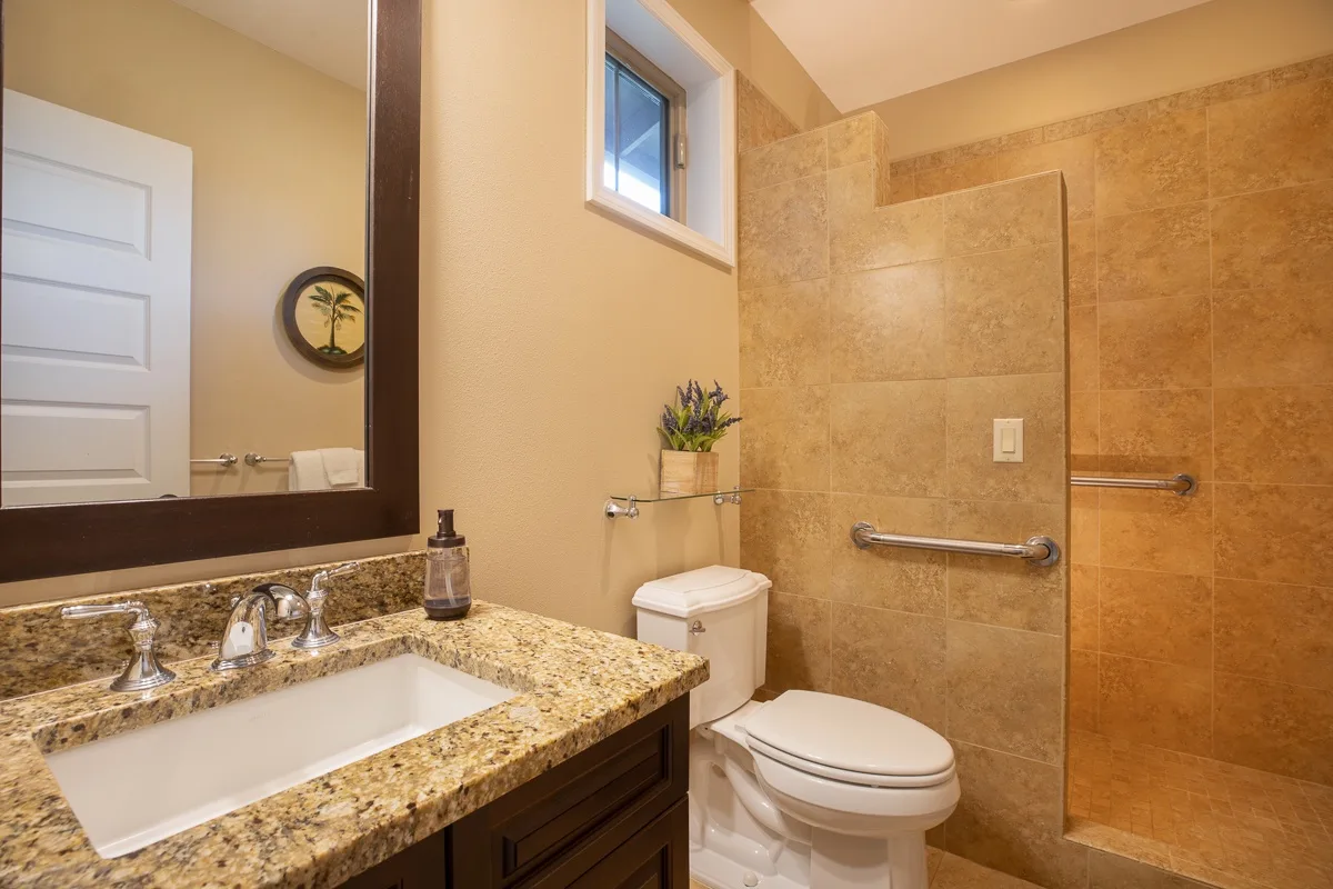 A bathroom with a sink vanity, toilet, and tiled shower area.