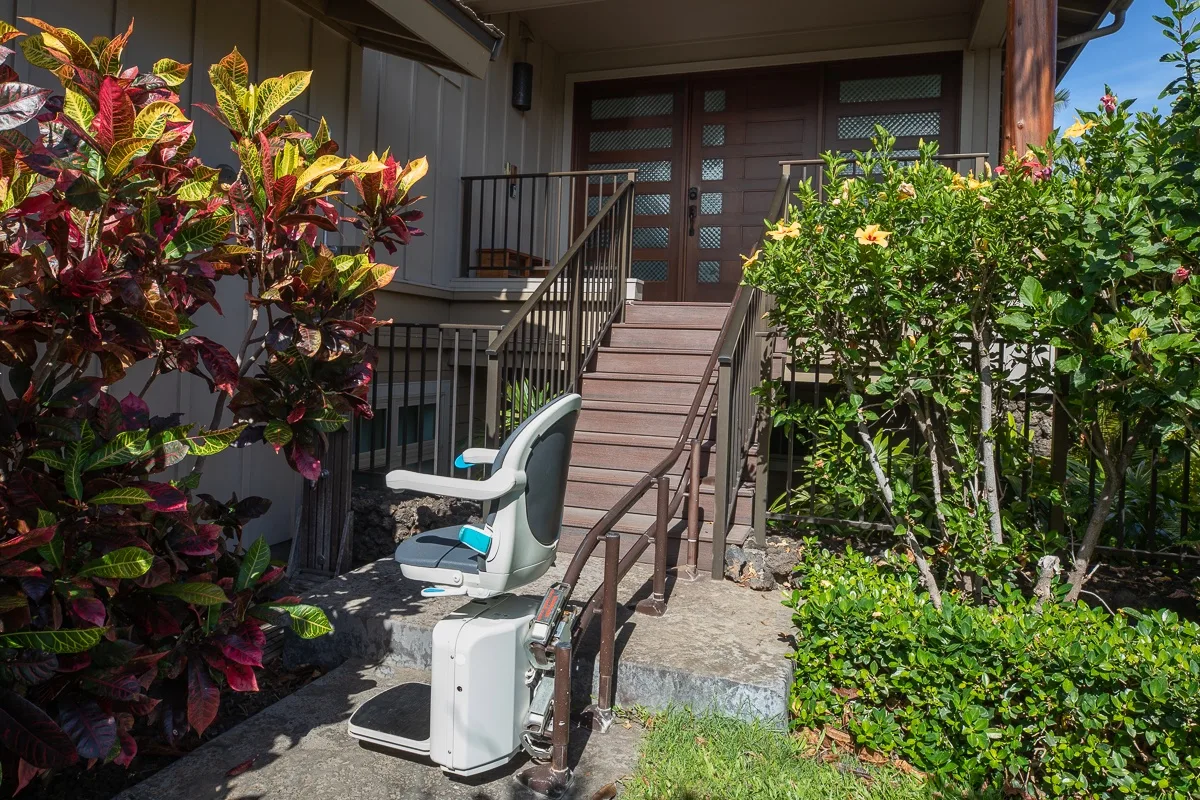 An exterior entrance with a ramp, handrails, and leafy plants.