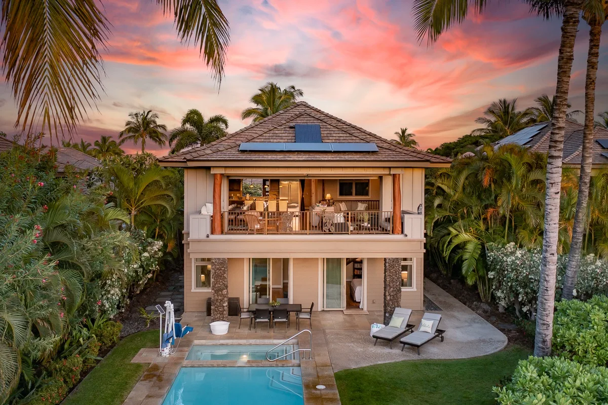 Una villa tropical de dos plantas da a una piscina bajo un cielo de atardecer colorido.
