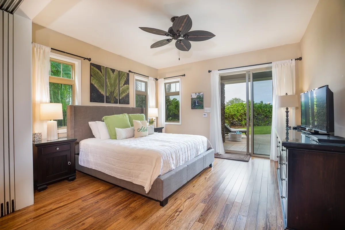 A bedroom with a bed, wood flooring, and sliding glass doors opening to greenery.