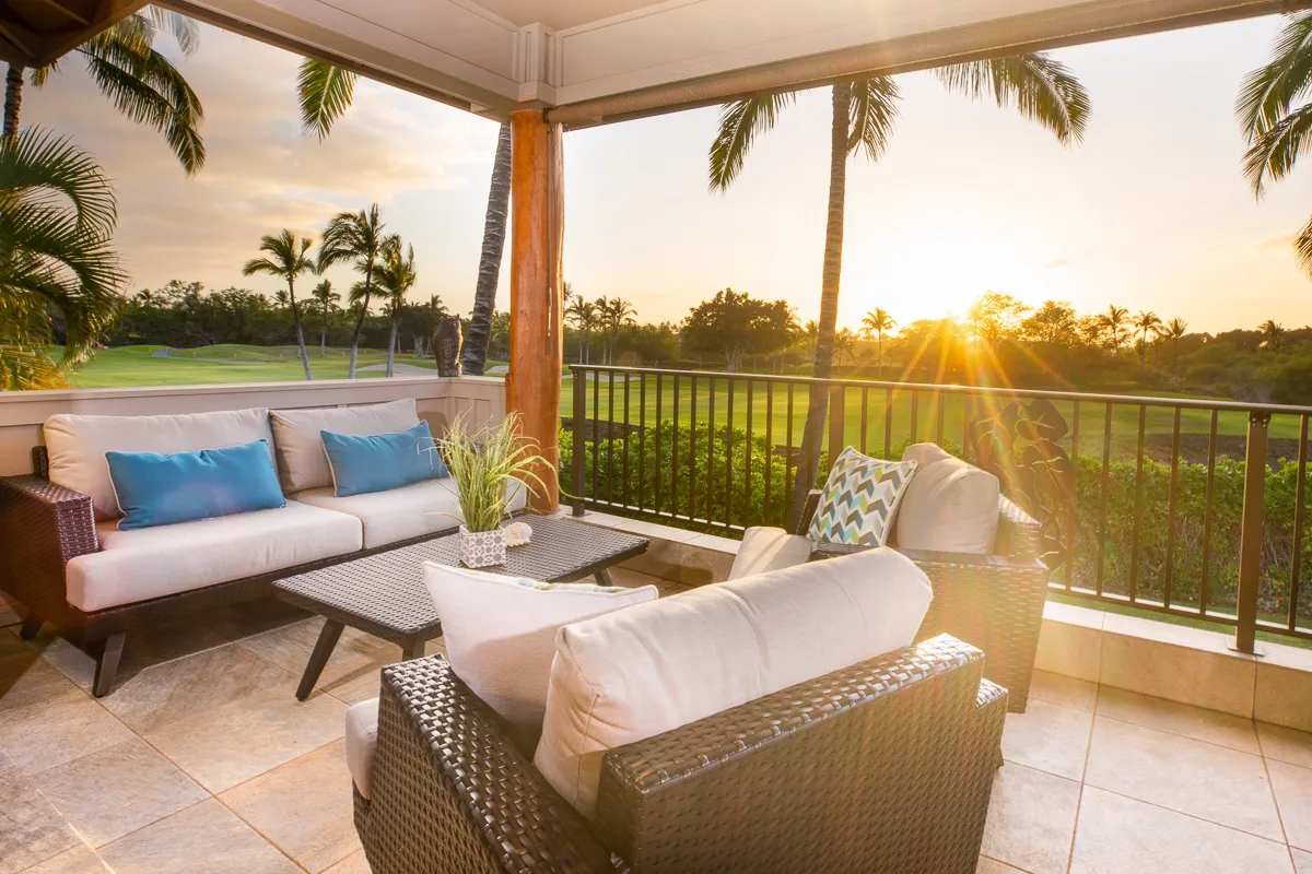 A covered patio seating area overlooks a palm-lined landscape at sunset.