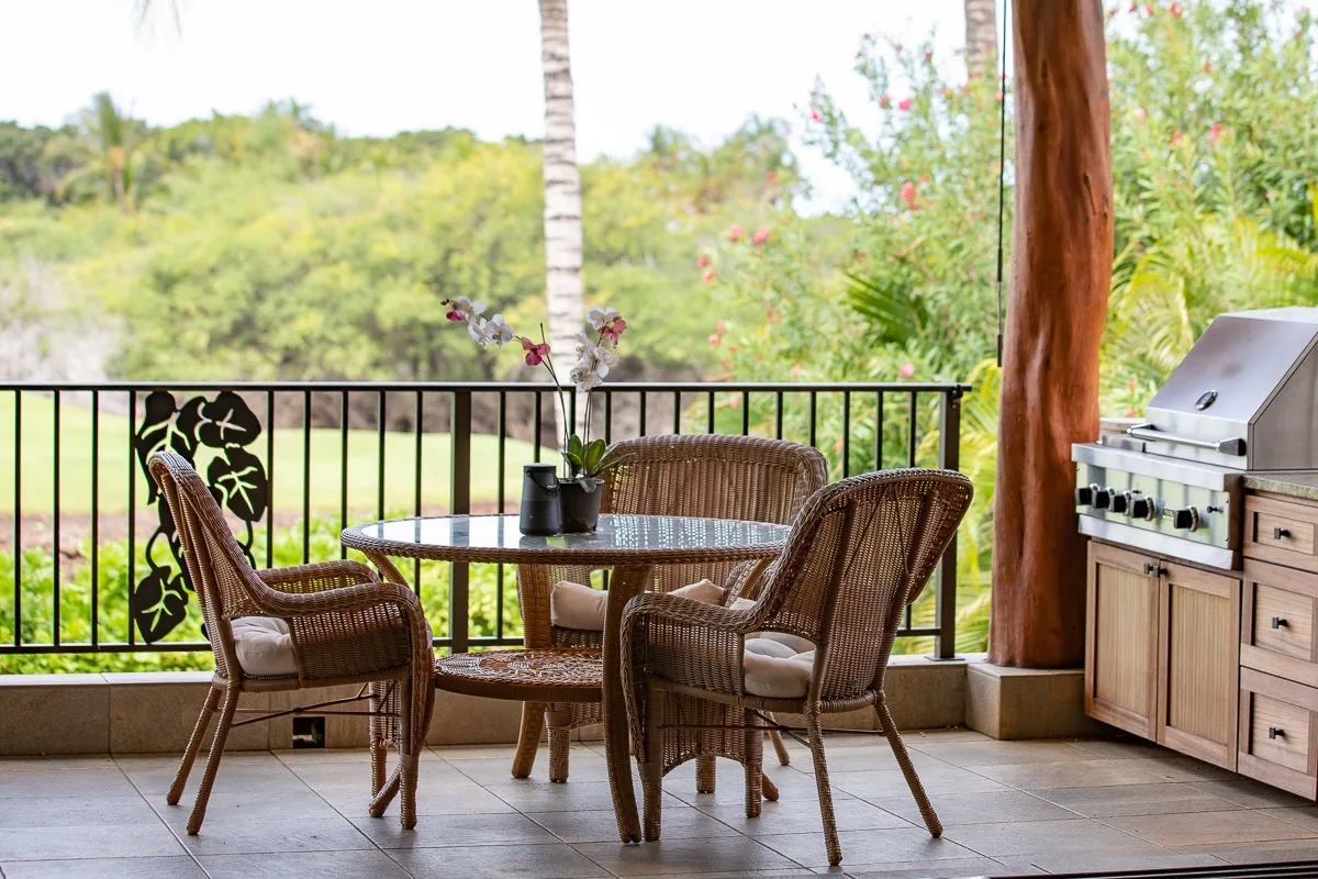 A covered patio has wicker seating, a small table, and an outdoor grill.