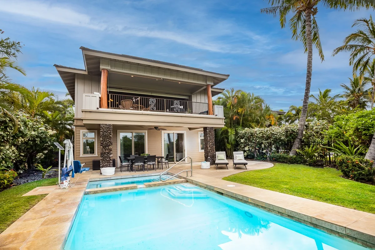 A tropical house overlooks a swimming pool, with a patio and garden.