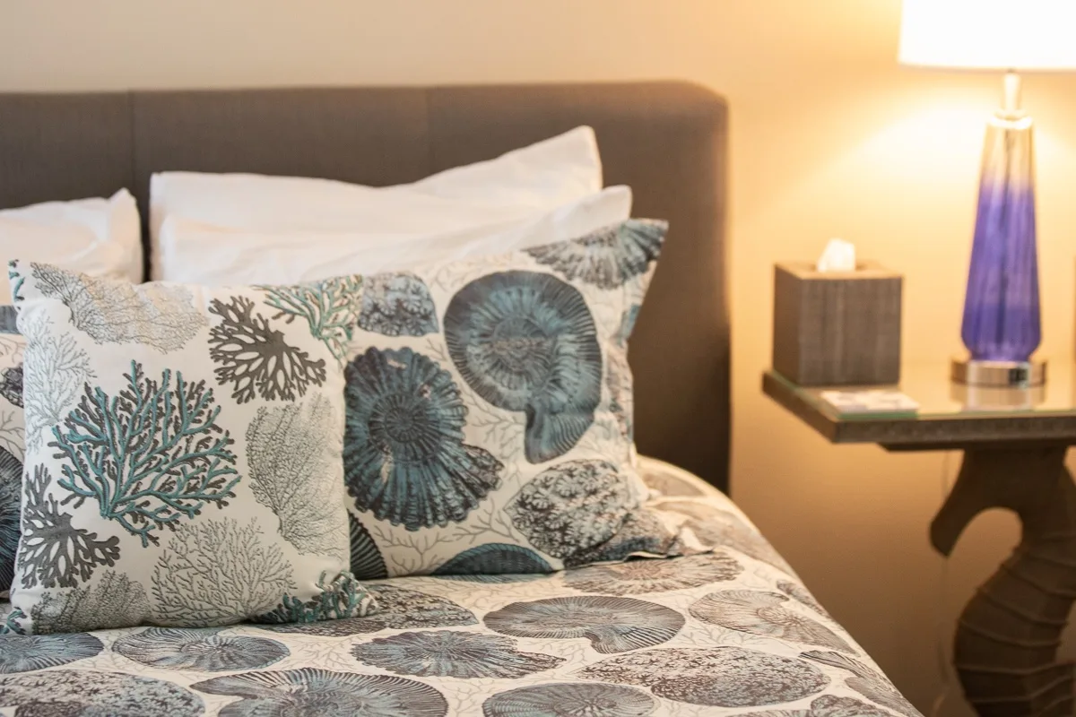 A bedroom with a bed dressed in patterned bedding and a lit bedside lamp.