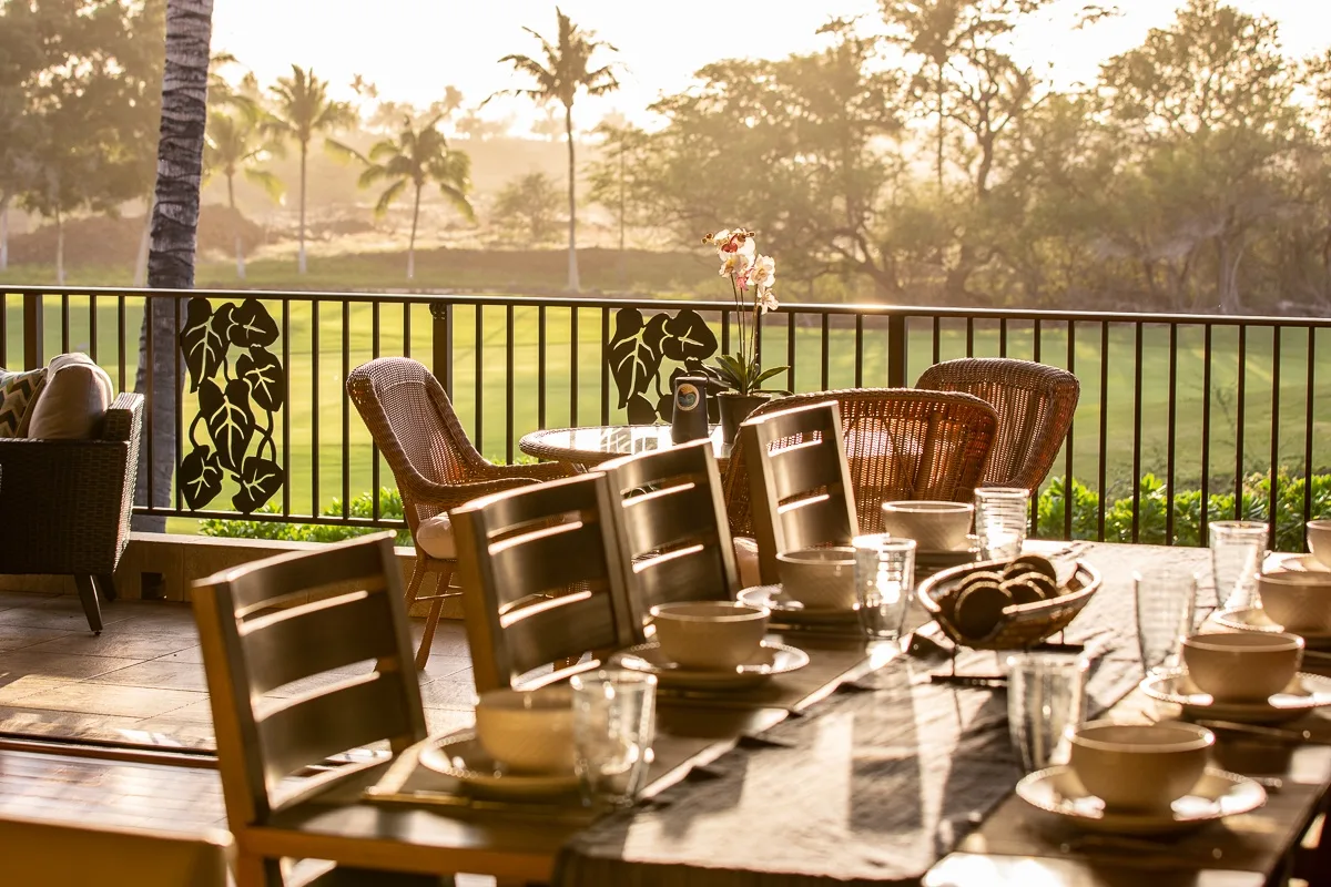 A sunlit outdoor dining area overlooks a green lawn and palm trees.