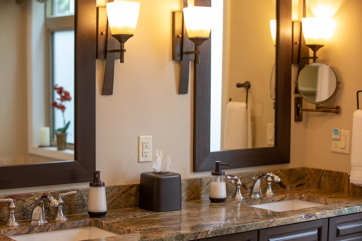 A bathroom vanity with a wide mirror, wall lights, and a stone countertop.