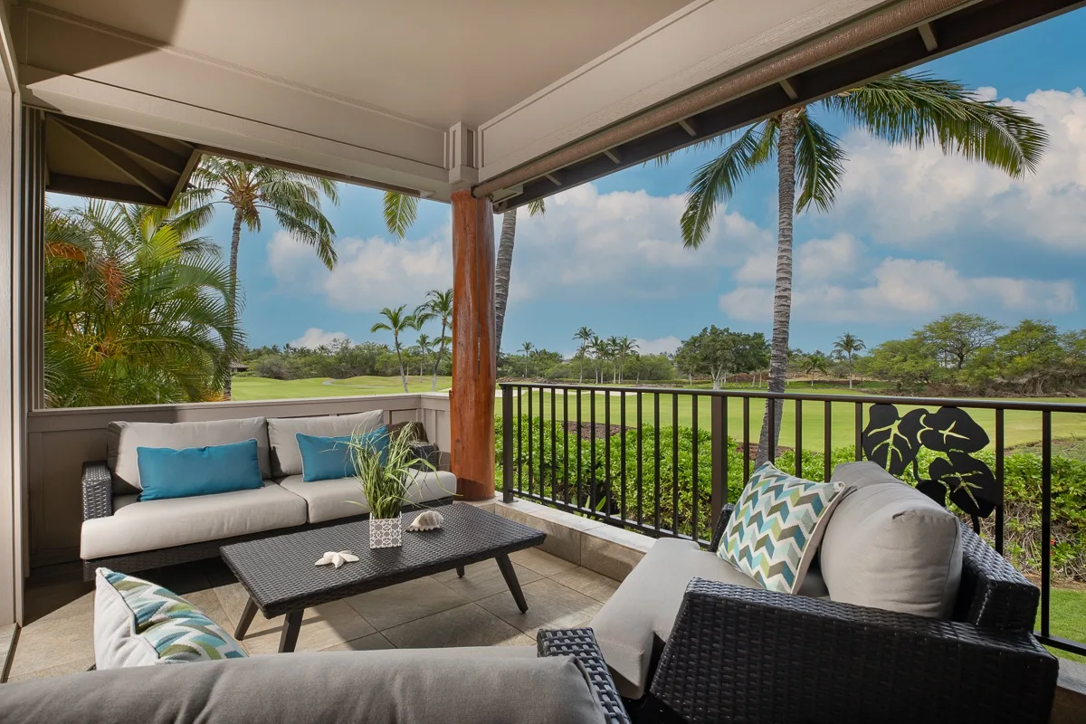 A covered outdoor seating area overlooks a green lawn and palm trees.