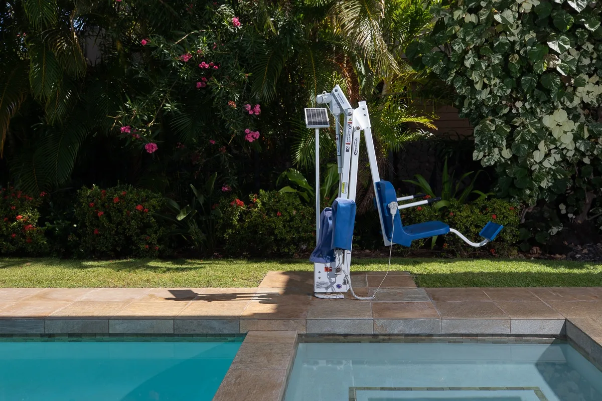 A poolside lift stands beside a swimming pool amid tropical greenery.