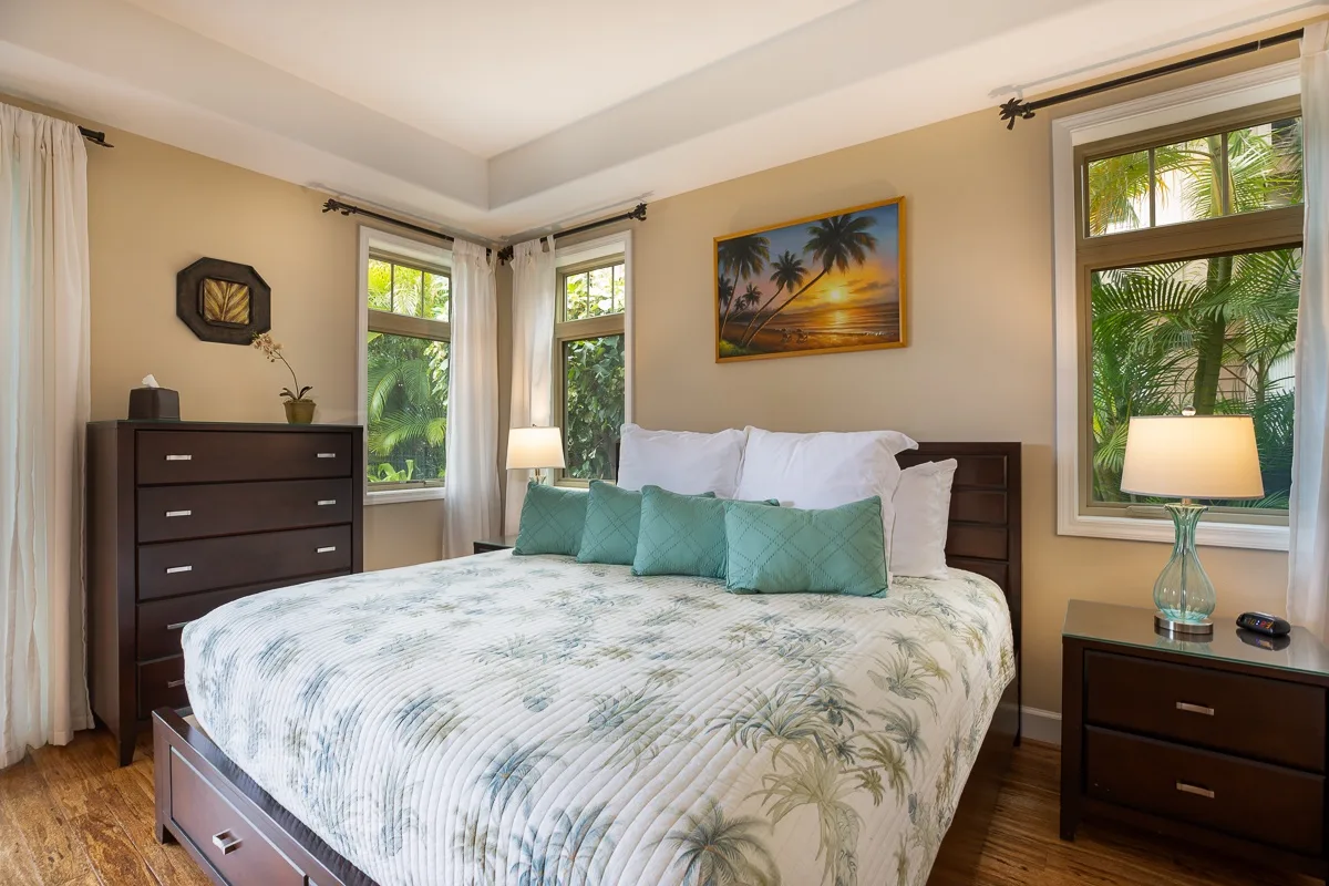 A bedroom with a bed dressed in white bedding and teal accent pillows.