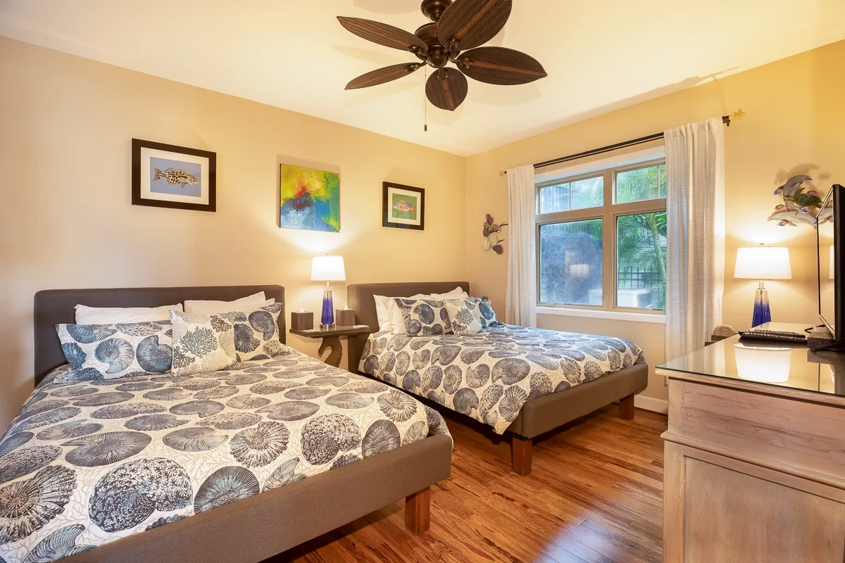 A bedroom with two beds, patterned bedding, and a window with light curtains.