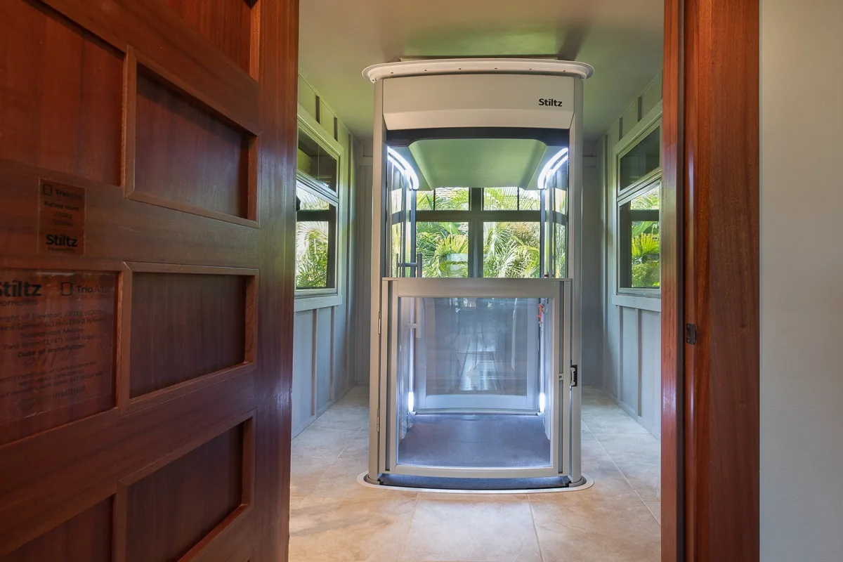 A compact glass elevator stands in a bright indoor entryway.