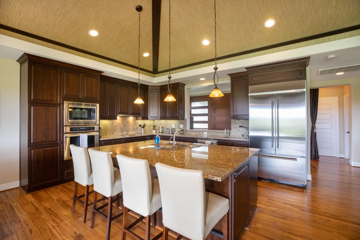 A kitchen with dark cabinets, stainless steel appliances, and a large island with seating.